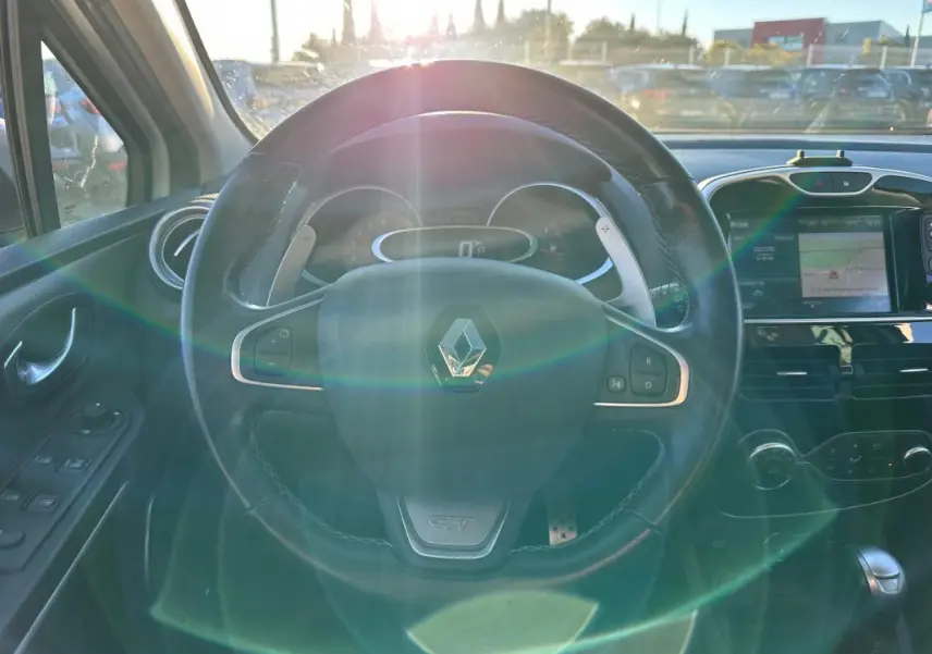 Vue intérieure centrée sur le volant cuir GT d'une Renault Clio IV blanche avec tableau de bord et écran tactile.