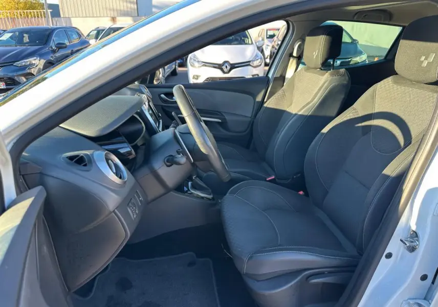 Intérieur avant droit d'une Renault Clio IV blanche, sièges noirs avec appuis-tête et volant cuir visible.