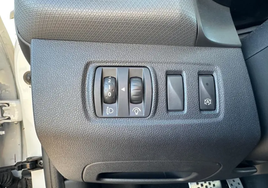 Gros plan sur les commandes de réglage d’éclairage et fonction arrêt auto du tableau de bord d’une Renault Clio IV blanche.