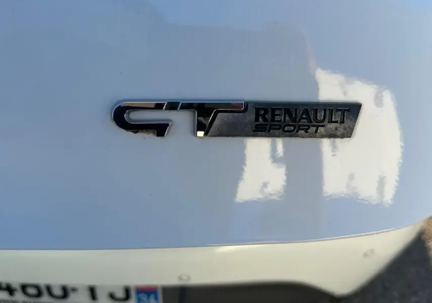 Gros plan sur l'emblème GT Renault Sport en chrome sur la carrosserie blanche arrière de la Renault Clio IV.