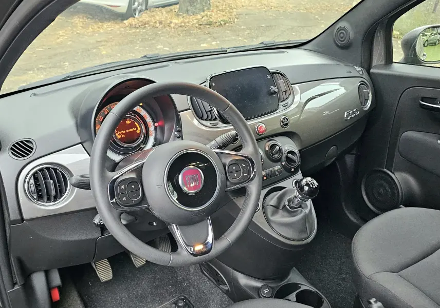 Intérieur côté conducteur de la FIAT 500 gris 2023, volant multifonction et tableau de bord moderne avec écran tactile.