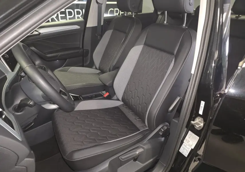 Vue intérieure côté conducteur du Volkswagen T-Roc noir, mettant en valeur les sièges tissu noir et gris avec coutures apparentes.