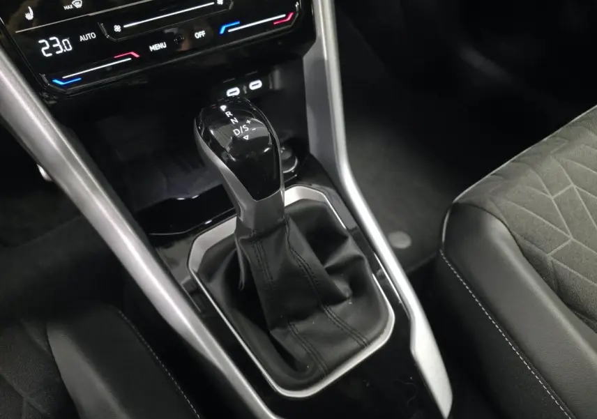 Gros plan sur la console centrale noire du Volkswagen T-Roc 2025 avec levier de vitesse automatique et sièges tissu gris.