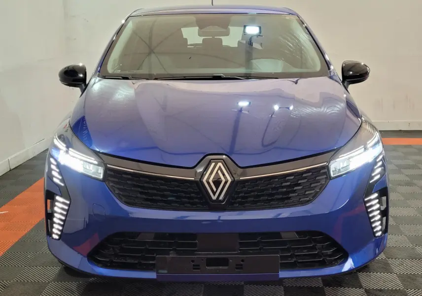 Vue frontale d'une Renault Clio Evolution Blue dCi 100 2025 bleu avec phares et feux LED allumés dans un intérieur neutre.