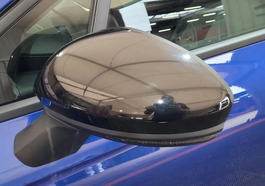 Rétroviseur côté gauche noir brillant sur Renault Clio bleu, avec reflet de l'environnement intérieur visible.