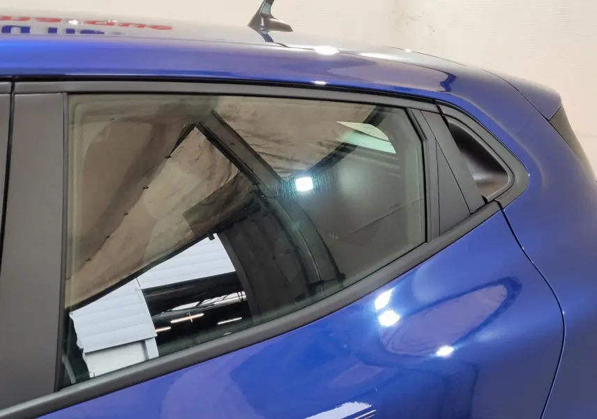 Vue côté gauche arrière d'une Renault Clio bleu brillant, mettant en valeur la ligne fluide et la vitre latérale arrière.
