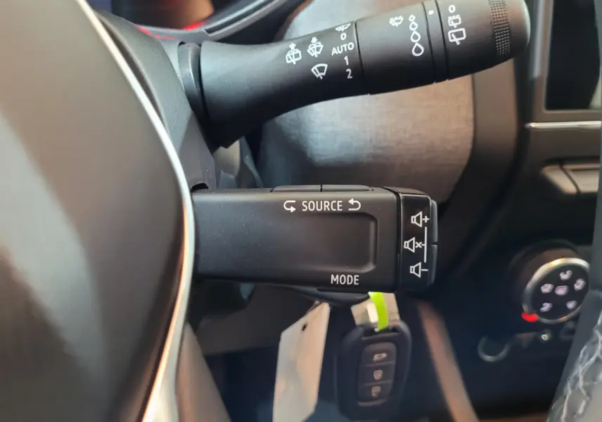 Gros plan sur la commande multifonctions à gauche du volant de la Renault Clio bleu, avec touches source et mode visibles.
