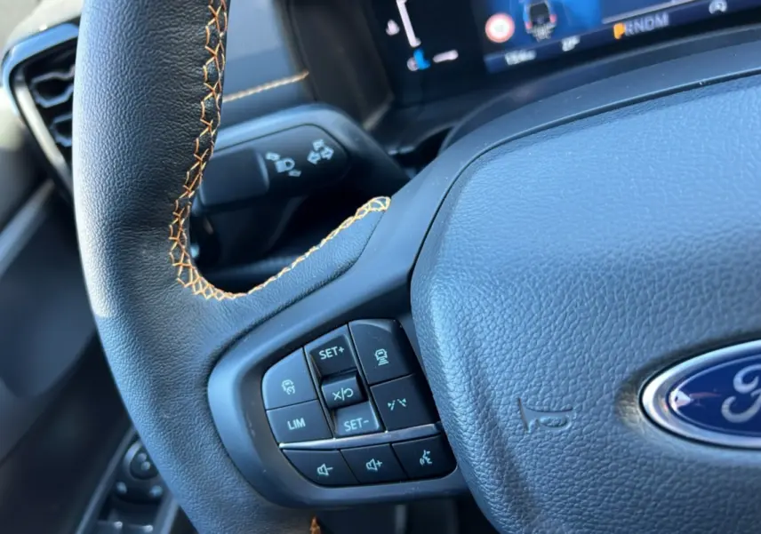 Gros plan sur le volant noir à surpiqûres orange du Ford Ranger 2025 avec commandes intégrées et logo Ford visible.