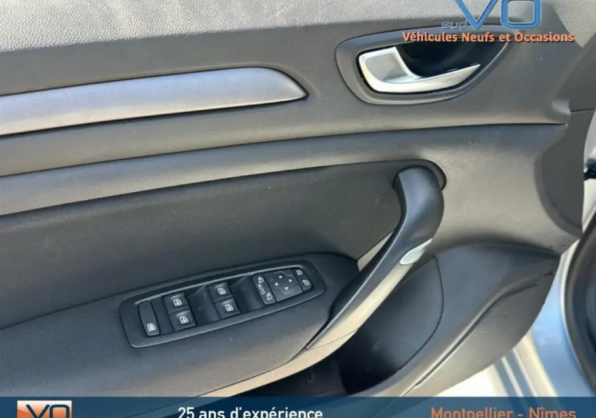 Détail de la porte avant gauche grise de la Renault Mégane IV Berline avec commandes électriques des vitres et poignée intérieure.