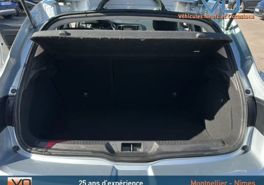 Coffre ouvert vu de l'arrière d'une Renault Mégane IV berline gris clair, montrant l'espace de chargement vide.