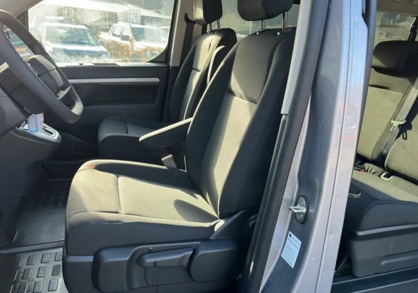 Vue intérieure côté conducteur du Peugeot Traveller gris acier 2025, montrant les sièges avant avec accoudoir central.