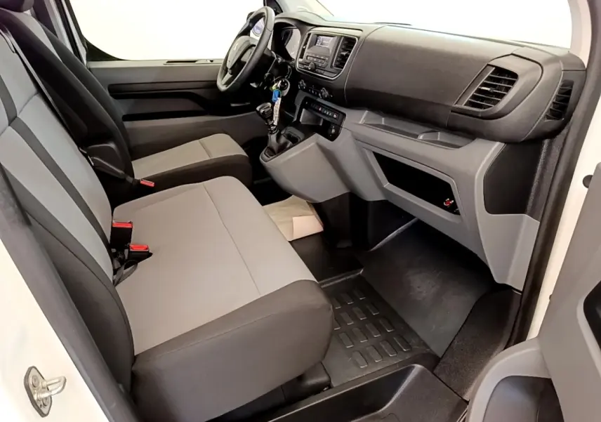 Vue intérieure côté conducteur du Peugeot Traveller 2018 blanc, montrant sièges gris et tableau de bord avec boîte manuelle.