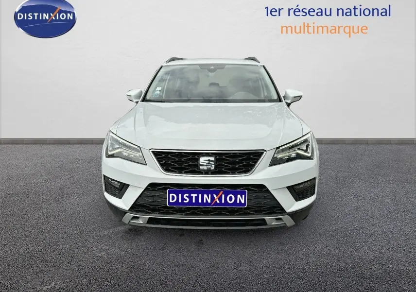 Vue frontale d'un SEAT Ateca blanc Nevada 2018 avec calandre noire et phares LED allumés sur fond neutre.