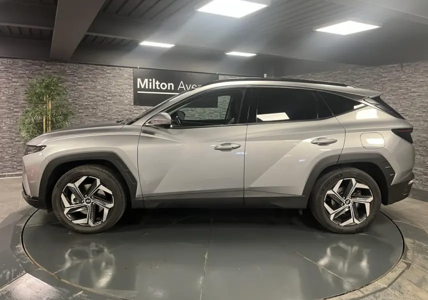 Vue de profil côté gauche du Hyundai Tucson gris métallisé 2023 avec jantes alliage et toit noir contrasté.