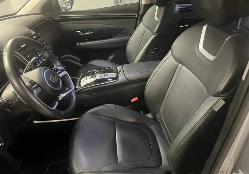Intérieur du Hyundai Tucson 2023 vu côté conducteur, sièges cuir noirs et console centrale moderne avec commandes tactiles.