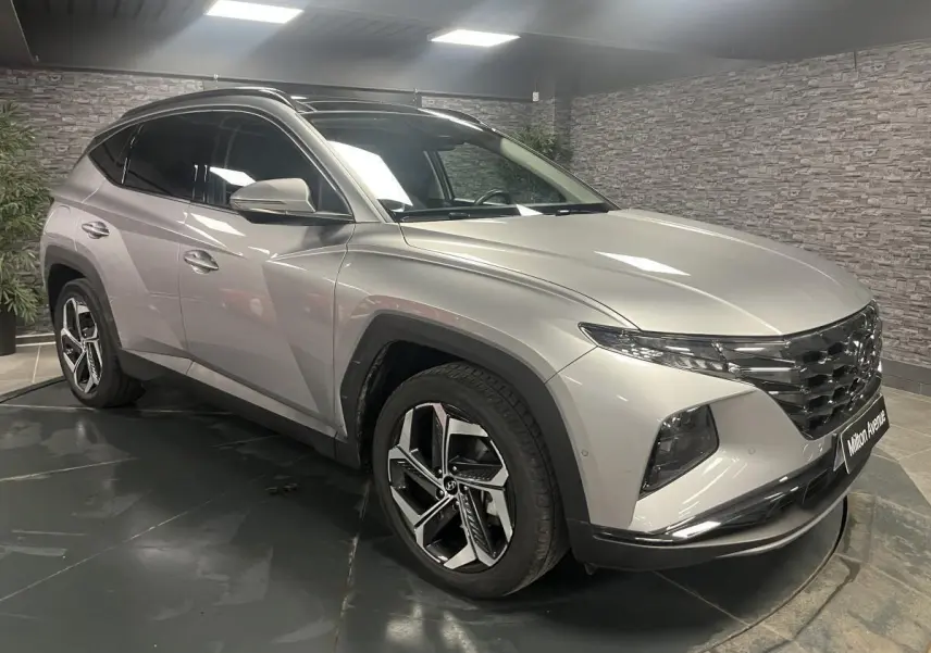 Vue 3/4 avant gauche d'un Hyundai Tucson gris métallisé avec calandre chromée et jantes alliage 19 pouces.