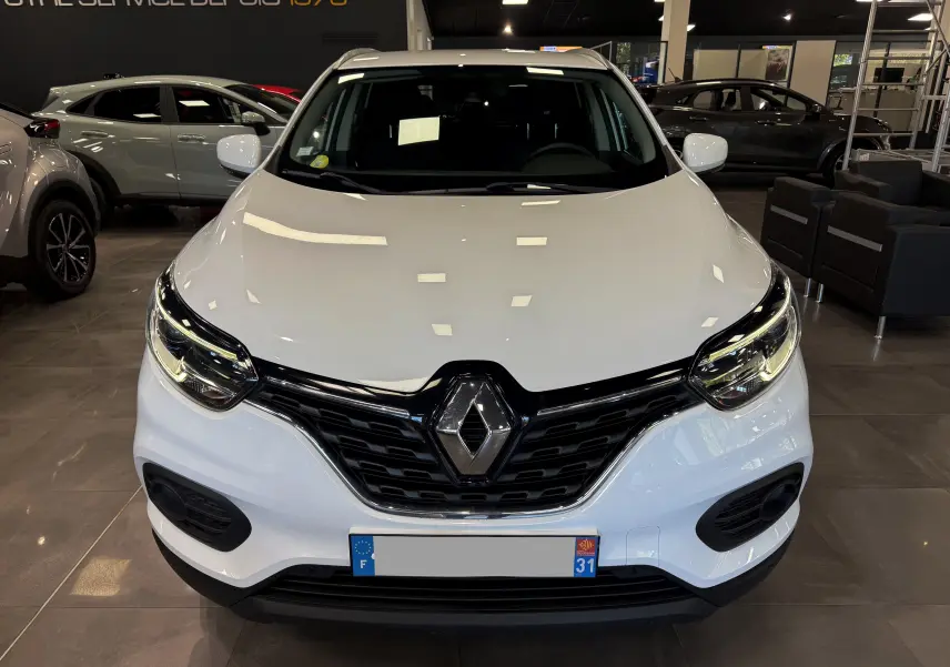 Vue frontale d'un Renault Kadjar blanc glacier 2020 en showroom, mettant en valeur sa calandre noire et ses phares LED.