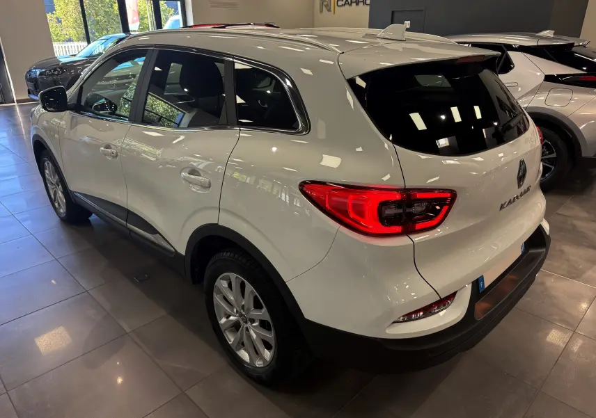 Vue 3/4 arrière droite d'un Renault Kadjar Blanc Glacier 2020 en showroom, avec feux arrière allumés et jantes alliage.
