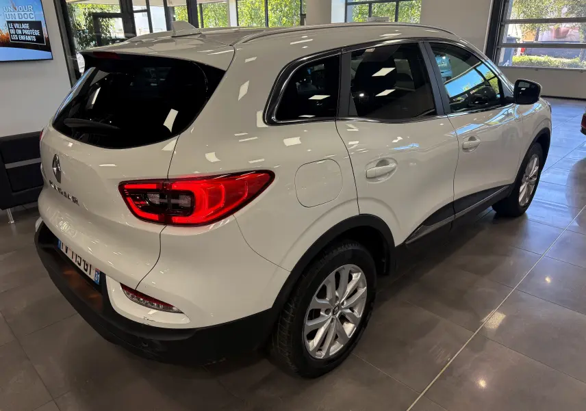 Vue 3/4 arrière droite du Renault Kadjar blanc glacier 2020 en showroom, avec feux arrière allumés et jantes alliage.