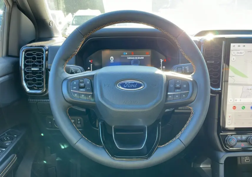 Vue intérieure centrée sur le volant du Ford Ranger 2025 gris iconic, avec tableau de bord numérique et écran tactile visible.