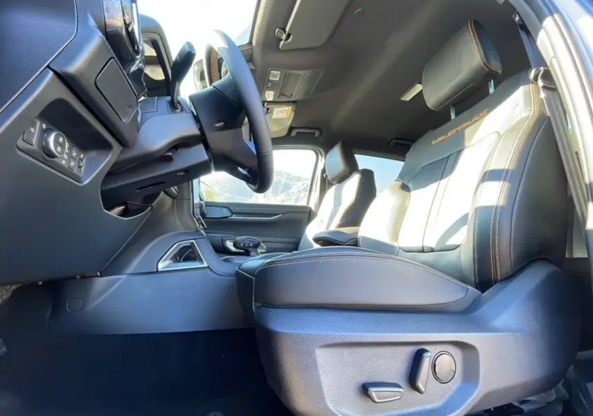 Intérieur du Ford Ranger 2025 Wildtrak Plus, vue côté conducteur sur les sièges noirs avec surpiqûres orange et volant.