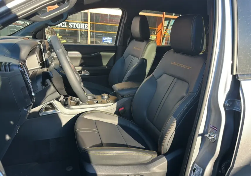 Vue intérieure côté conducteur du Ford Ranger 2025 gris iconic, sièges en cuir avec logo Wildtrak brodé et surpiqûres orange.
