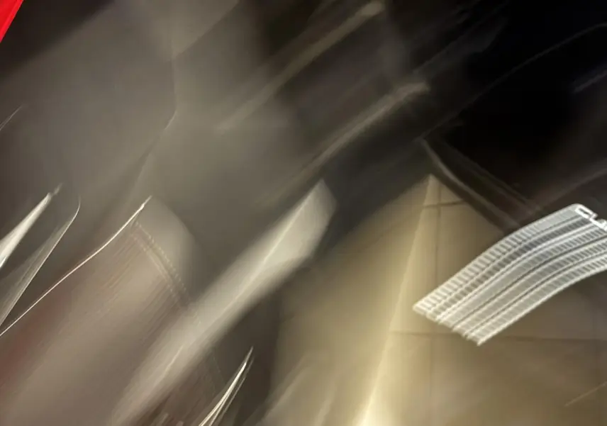 Détail flou du siège avant en suédine noire avec surpiqûres cuivrées et logo CUPRA lumineux projeté au sol.