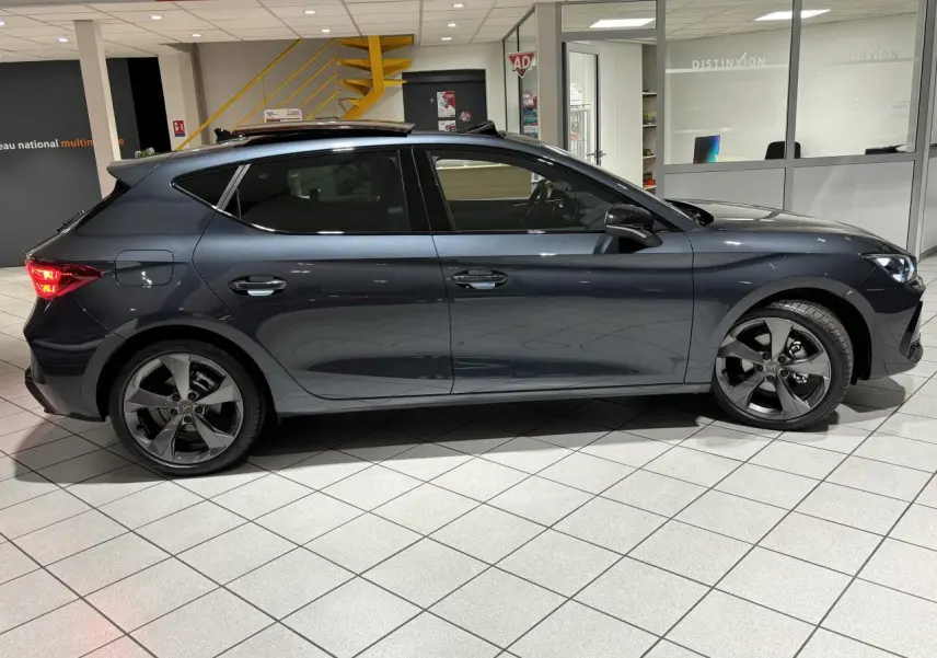 Vue de profil côté gauche d'une CUPRA Leon gris Graphène avec jantes alliage 18 pouces et toit ouvrant panoramique.