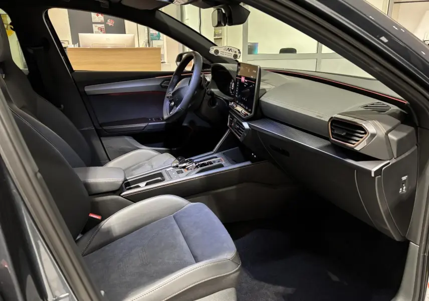 Vue intérieure côté conducteur de la CUPRA Leon 2026 gris Graphène avec sièges suédine noirs et tableau de bord moderne.