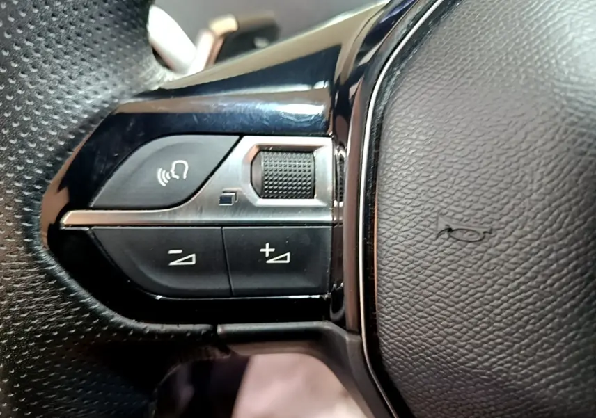 Gros plan sur les commandes multifonctions en plastique noir et chrome du volant cuir du Peugeot 3008 gris foncé.
