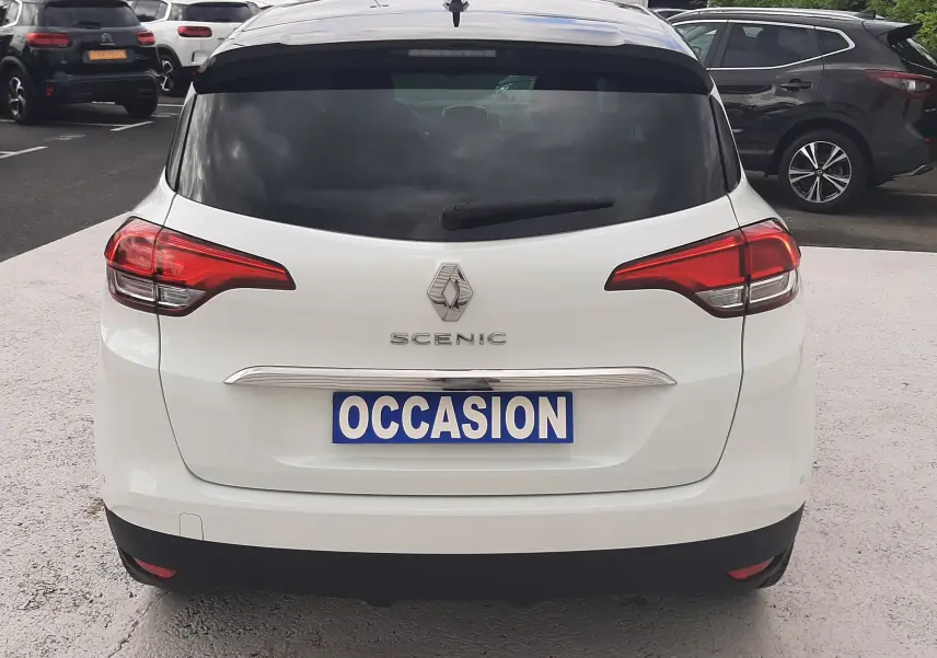 Vue arrière d'un Renault Scénic IV blanc nacré avec toit noir, plaque "OCCASION" visible sur un parking extérieur.