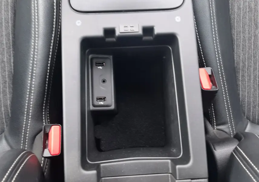 Vue plongeante sur la console centrale ouverte du Renault Scenic IV, avec ports USB et sièges noirs à surpiqûres blanches.