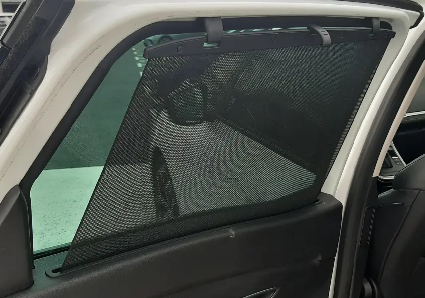 Vue intérieure du côté gauche arrière d'un Renault Scenic IV blanc nacré avec store pare-soleil noir fixé à la porte ouverte.
