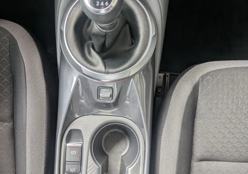 Vue plongeante sur la console centrale du Nissan Juke rouge 2020, avec levier de vitesse manuel et bouton Start/Stop visibles.