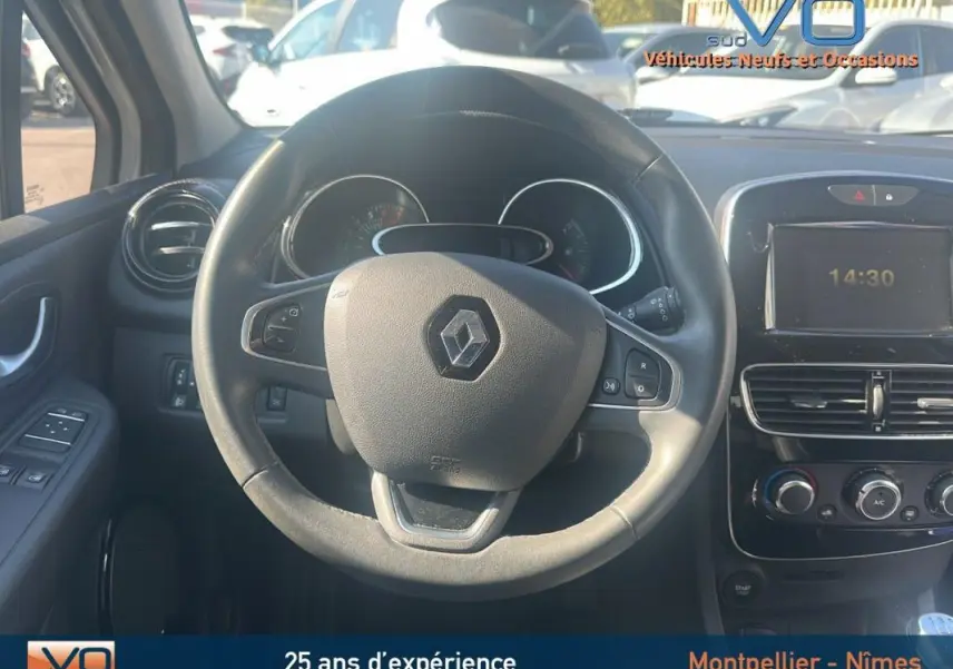 Vue intérieure centrée sur le volant cuir de la Renault Clio IV Estate Business blanche, avec tableau de bord et commandes visibles.