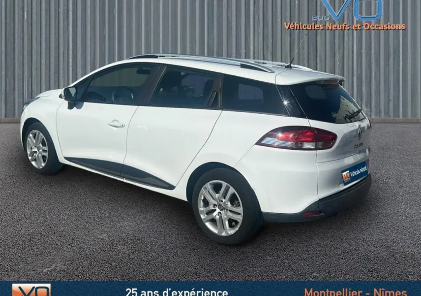 Vue 3/4 arrière droite d'une Renault Clio IV Estate Business blanche avec vitres surteintées et barres de toit.