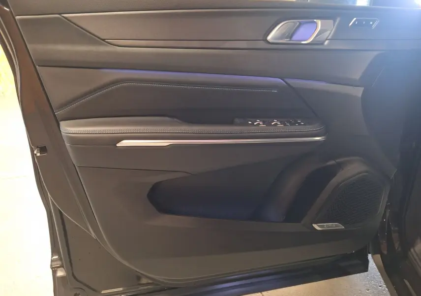 Vue intérieure de la porte avant gauche noire du Lynk & Co 01 PHEV avec haut-parleur intégré et commandes électriques.