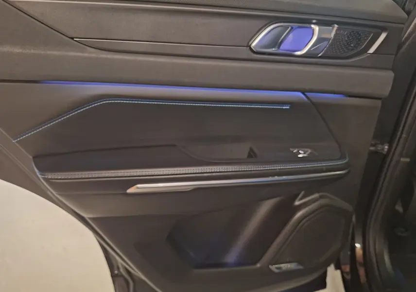 Gros plan sur la porte arrière droite noire du Lynk & Co 01 avec éclairage d’ambiance bleu et surpiqûres bleues.