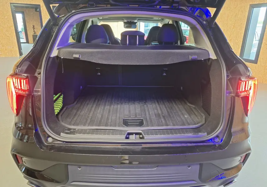 Vue arrière du coffre ouvert du LYNK & CO 01 noir avec tapis de coffre marqué et feux arrière allumés.