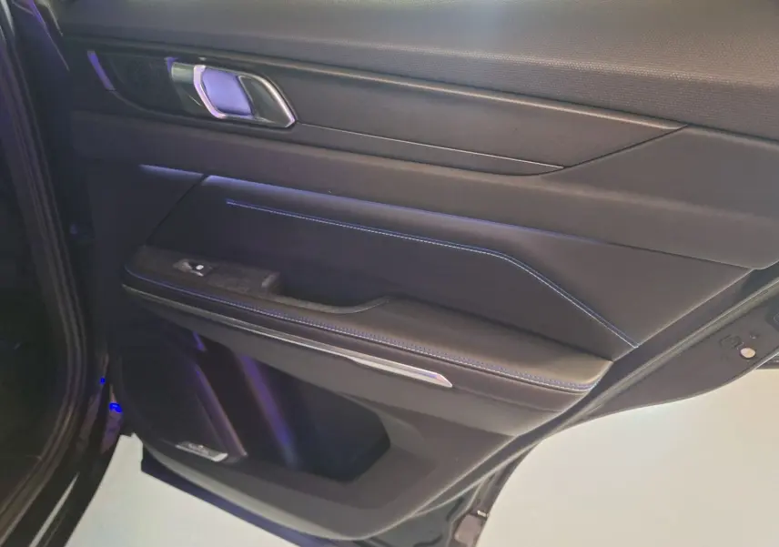 Gros plan sur la porte arrière droite noire du LYNK & CO 01 PHEV avec surpiqûres bleues et poignée chromée.