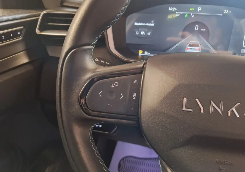 Gros plan sur le volant noir de la Lynk & Co 01 avec commandes multifonctions et tableau de bord digital en arrière-plan.