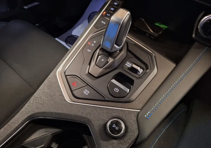 Gros plan sur la console centrale du Lynk & Co 01 PHEV 261 DCTH7 noire, avec levier de vitesse et surpiqûres bleues.