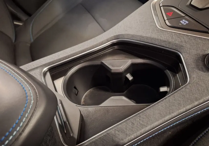 Gros plan sur le porte-gobelets noir et l'accoudoir central avec surpiqûres bleues dans l'habitacle du Lynk & Co 01 PHEV.
