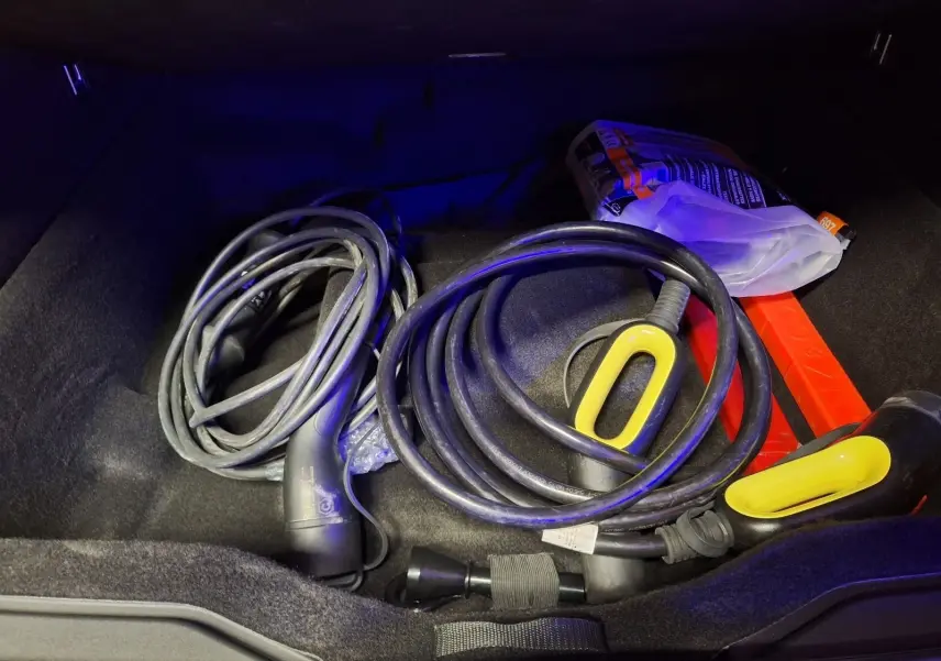 Coffre ouvert d'un Lynk & Co 01 noir 2022, montrant câbles de recharge hybrides et accessoires rangés.