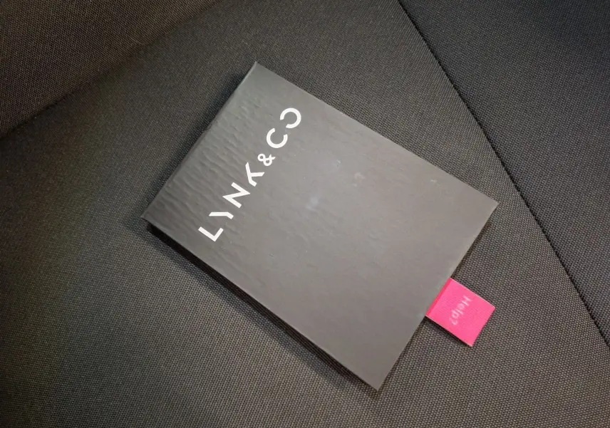 Manuel d'utilisation noir de la marque LYNK & CO posé sur un siège en tissu gris foncé.