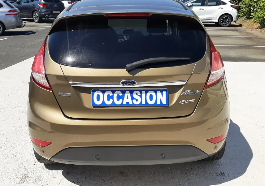 Vue arrière d'une Ford Fiesta marron métal de 2013 avec hayon fermé et plaque "OCCASION" visible.
