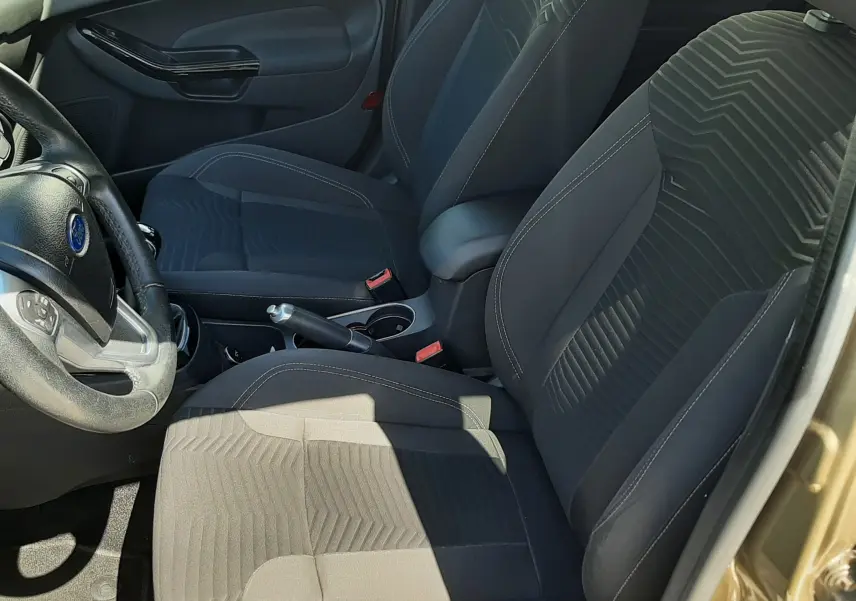 Vue intérieure côté conducteur de la Ford Fiesta 2013, sièges tissu noir avec motifs géométriques et volant multifonction.
