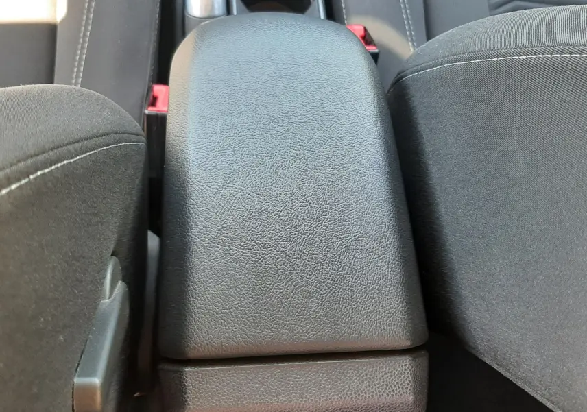 Vue rapprochée de l'accoudoir central noir en cuir et tissu entre les sièges avant d'une Ford Fiesta marron métal.