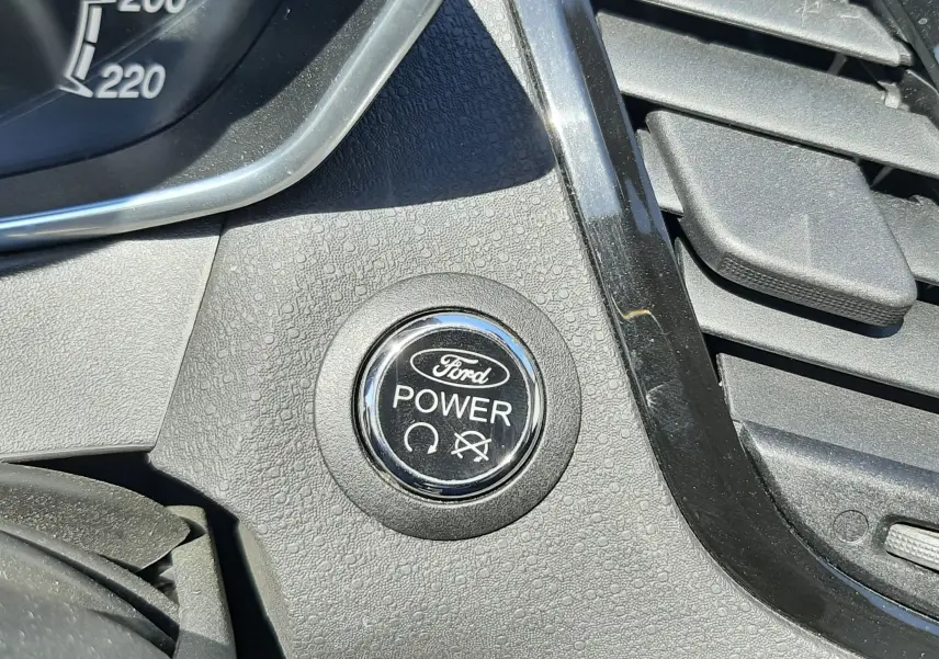 Gros plan sur le bouton Ford Power du tableau de bord côté gauche, entouré de plastique texturé noir.