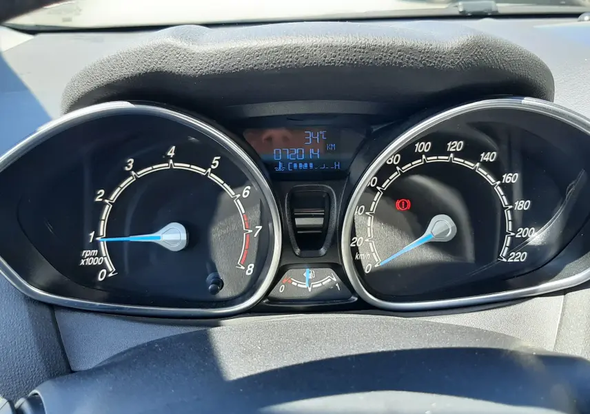 Vue rapprochée du tableau de bord noir de la Ford Fiesta marron, affichant compte-tours, vitesse et température extérieure à 34°C.